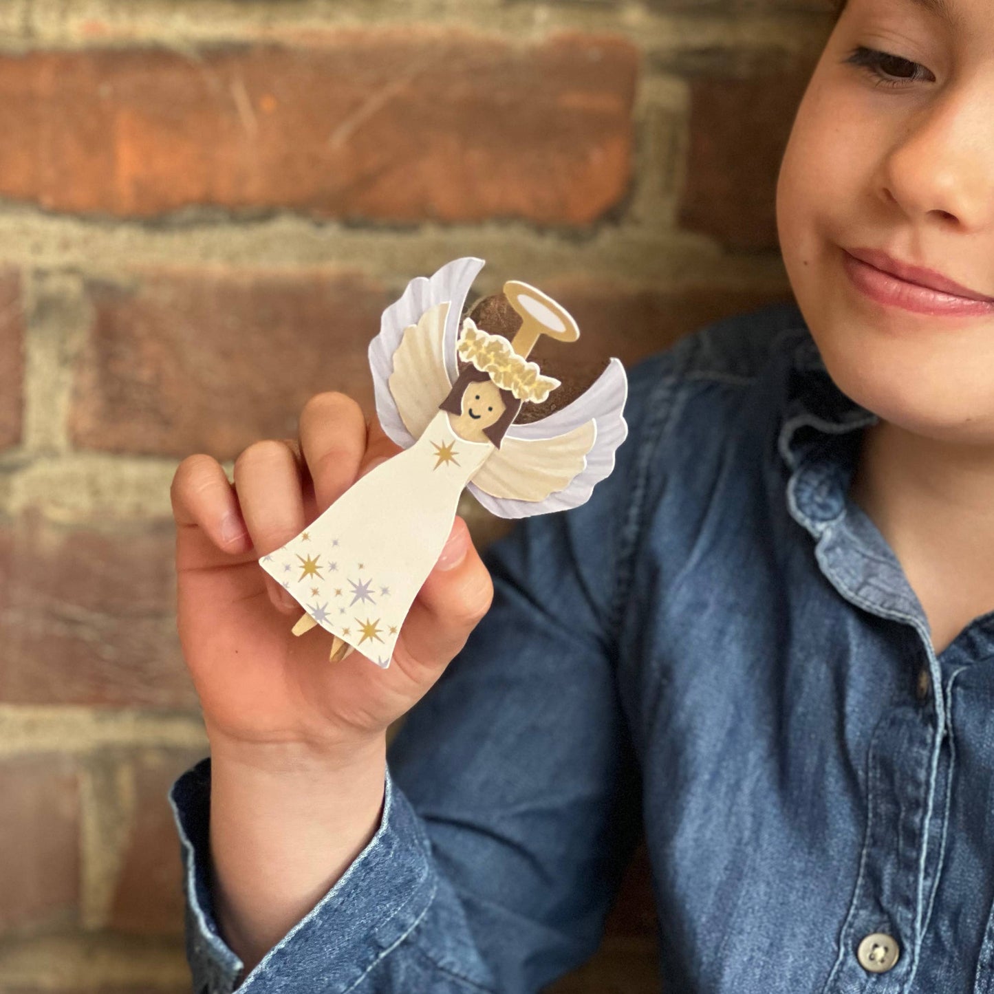 Child holding a small angel figurine against a brick wall background