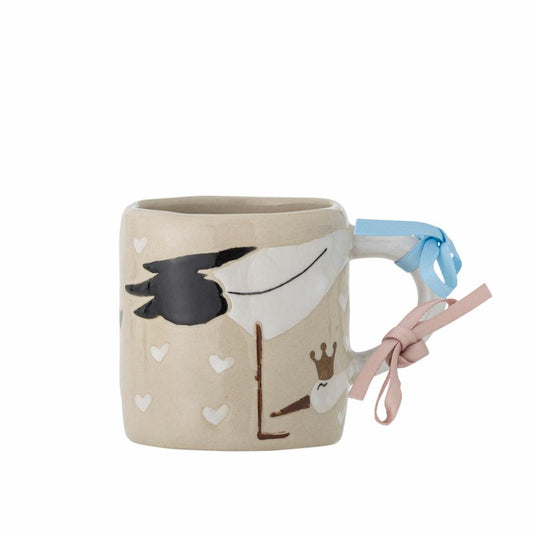 A beige stoneware mug with a stork design wrapping around the handle, accompanied by pink and blue ribbons.