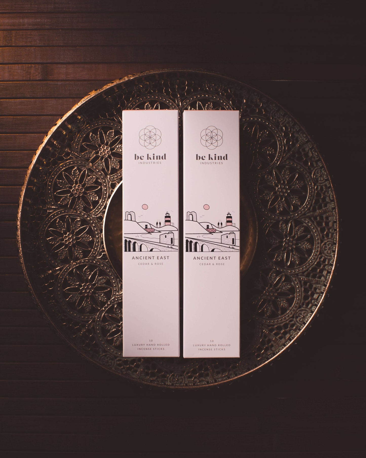 Two packs of Be Kind brand incense sticks, labeled 'Ancient East' placed side by side on a boho tray on a wooden table