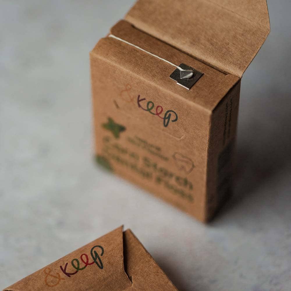 A cardboard dental floss dispenser with a small cutting blade. The package has the brand name '&keep' printed on it and is labeled as 'Vegan Cornstarch Floss' with 'Mint' indicated.