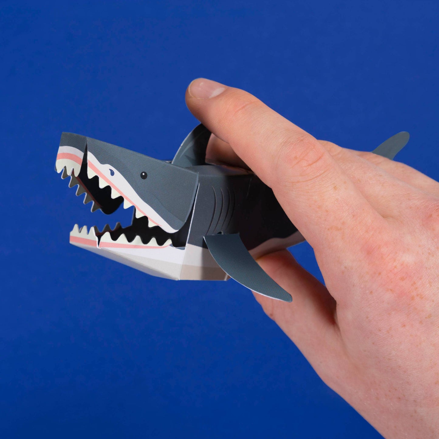 Hand holding a shark-shaped paper clip against a blue background
