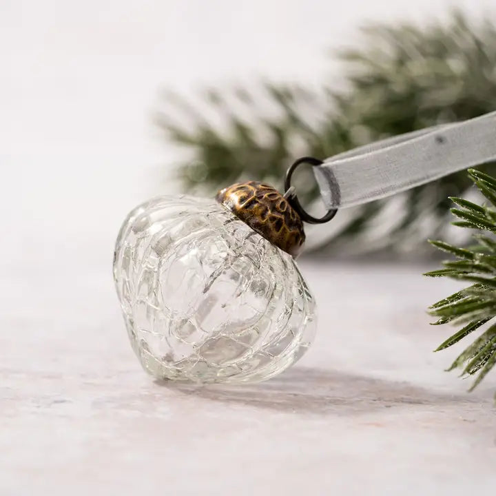 Clear glass lantern ornament with gold top on a white surface with greenery in the background
