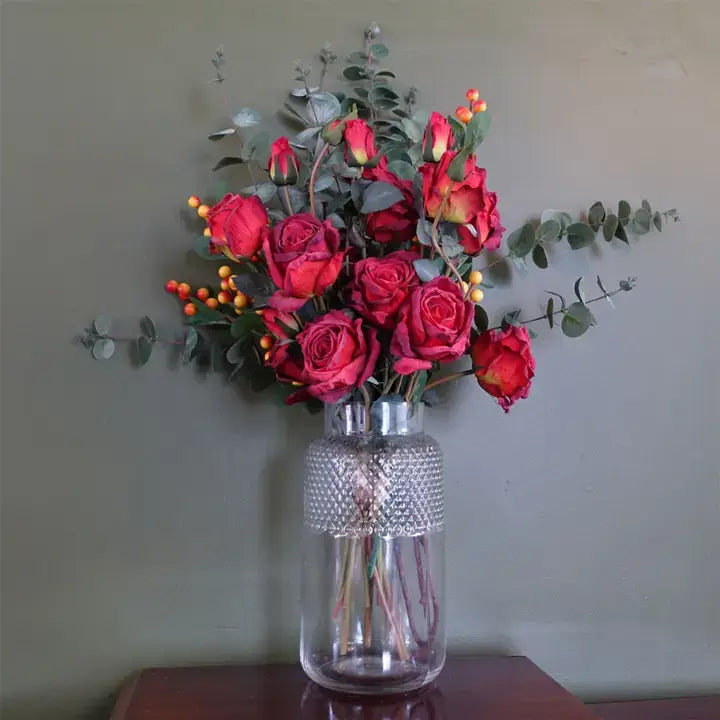 A clear glass vase with a geometric diamond pattern filled with red flowers.