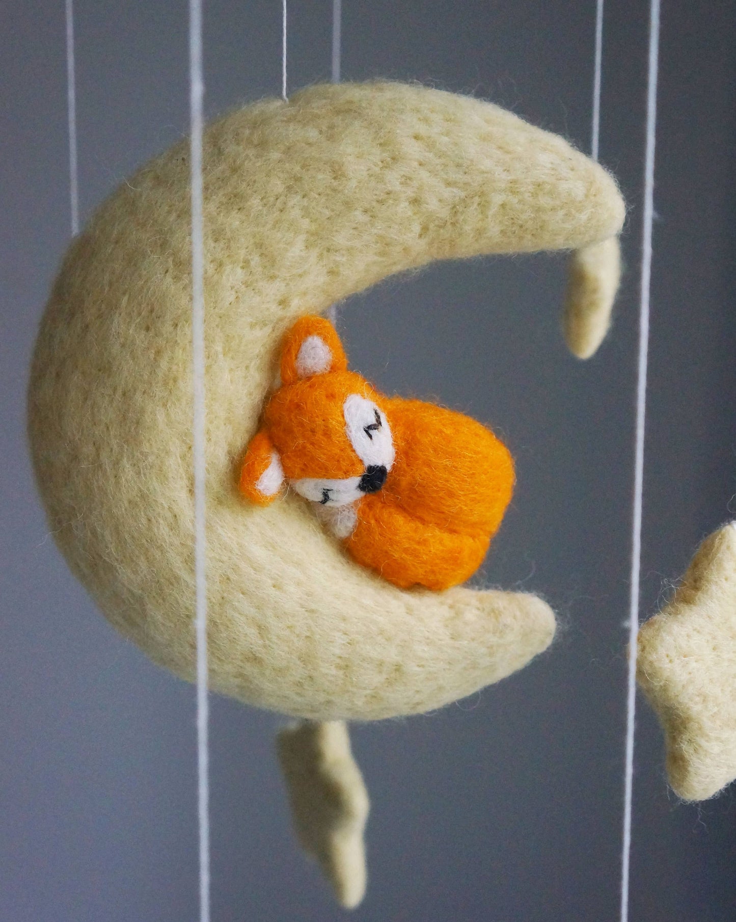 Felted fox toy on a felted moon mobile against a gray background