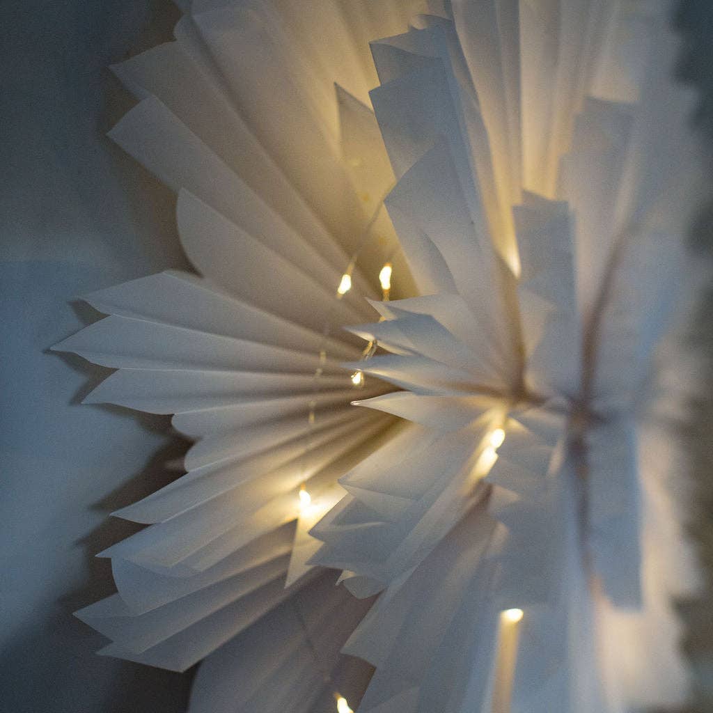 Close up view of paper flower decoration with fairy lights on grey wall