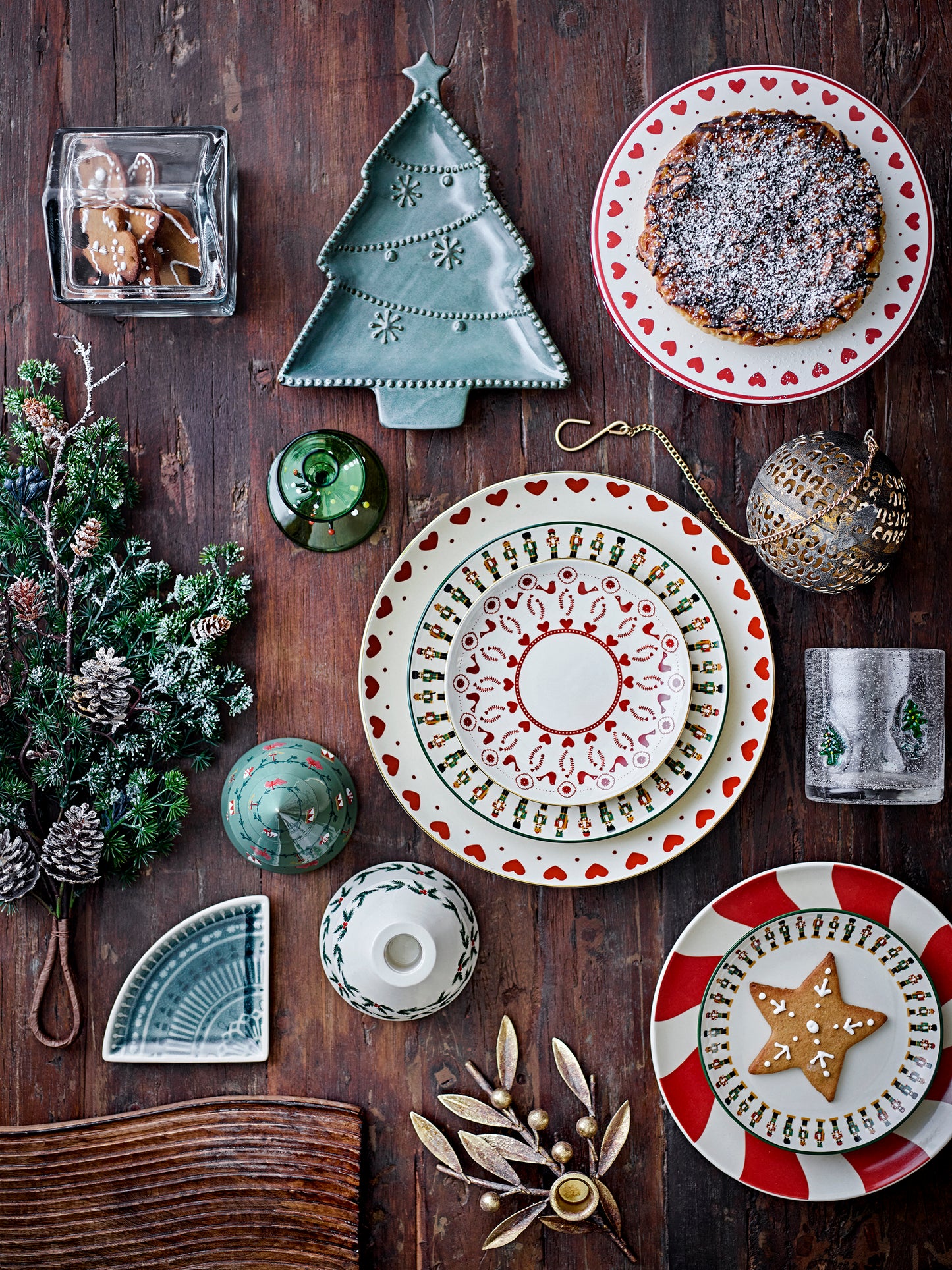 Decorative table setting with plates, ornaments, and a Christmas tree on a wooden surface.