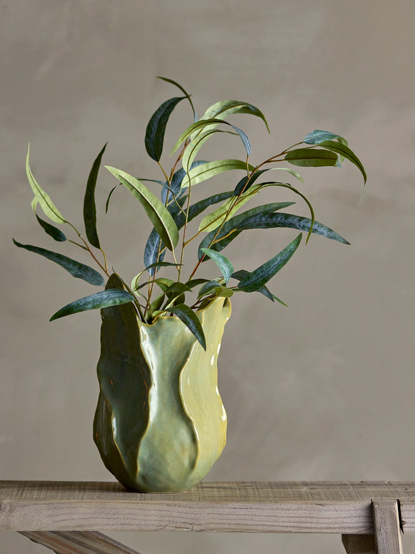 Green ceramic vase with leaves on a wooden surface against a plain background