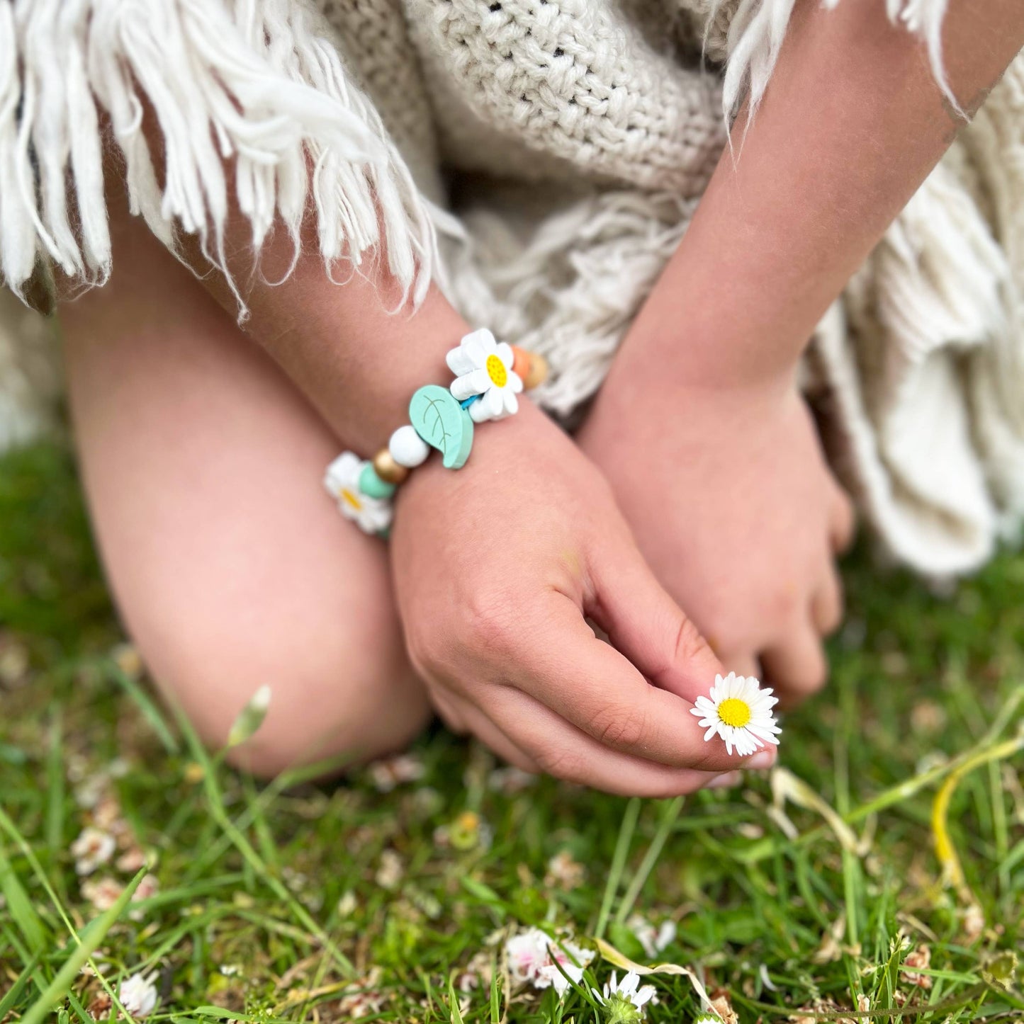 Child's hands wearing a bracelet with flowers on grass