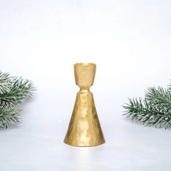 Gold coloured candle stick on a white background with greenery