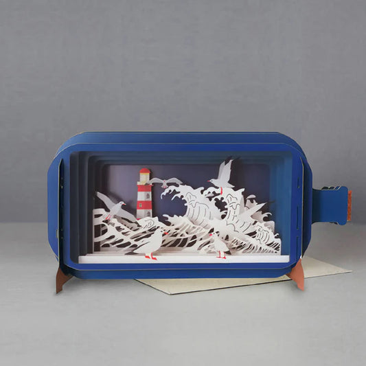 Pop up card in the shape of a bottle with the paper cut scene of crashing waves, seagulls and a lighthouse