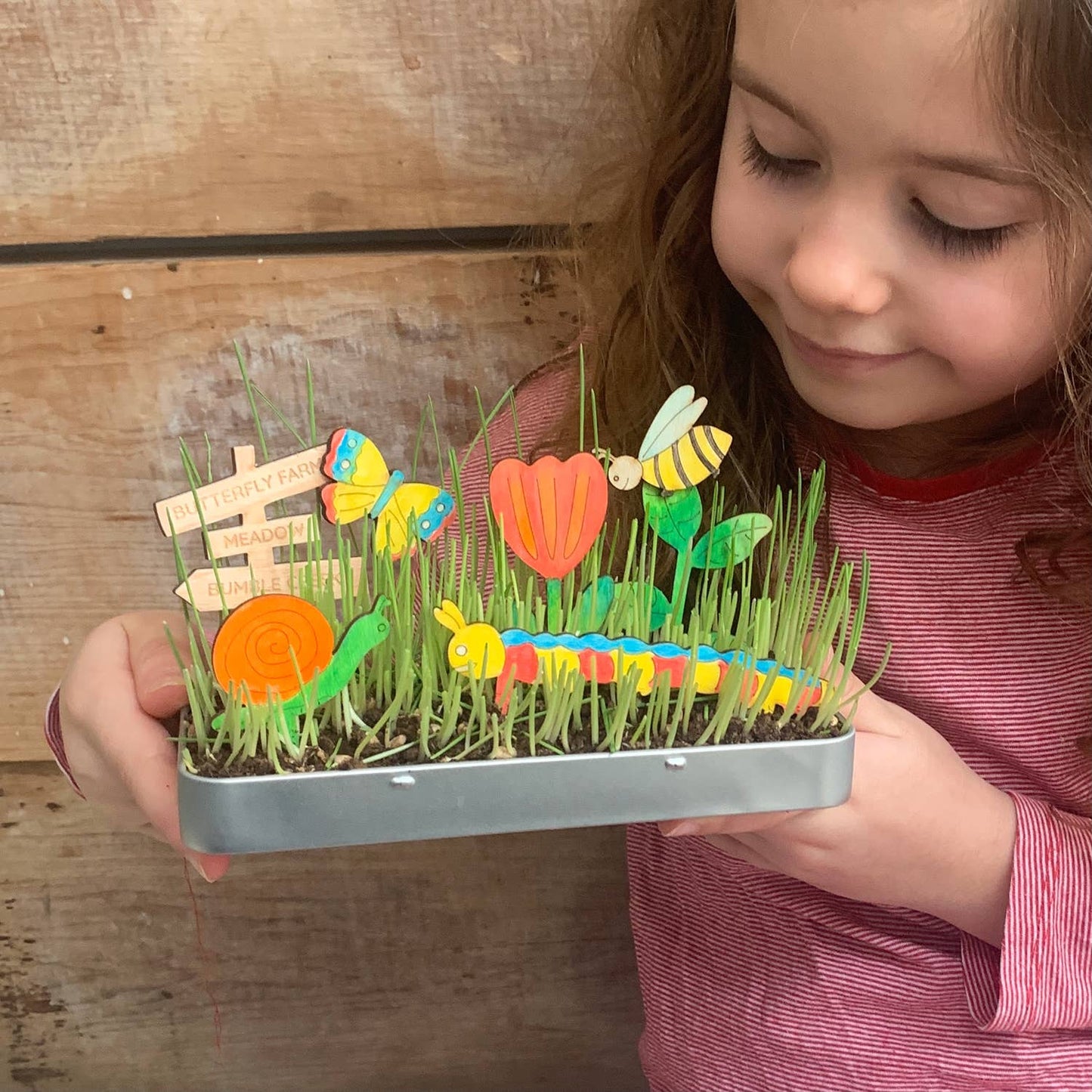 Child holding a small garden with toy plants and animals against a wooden background