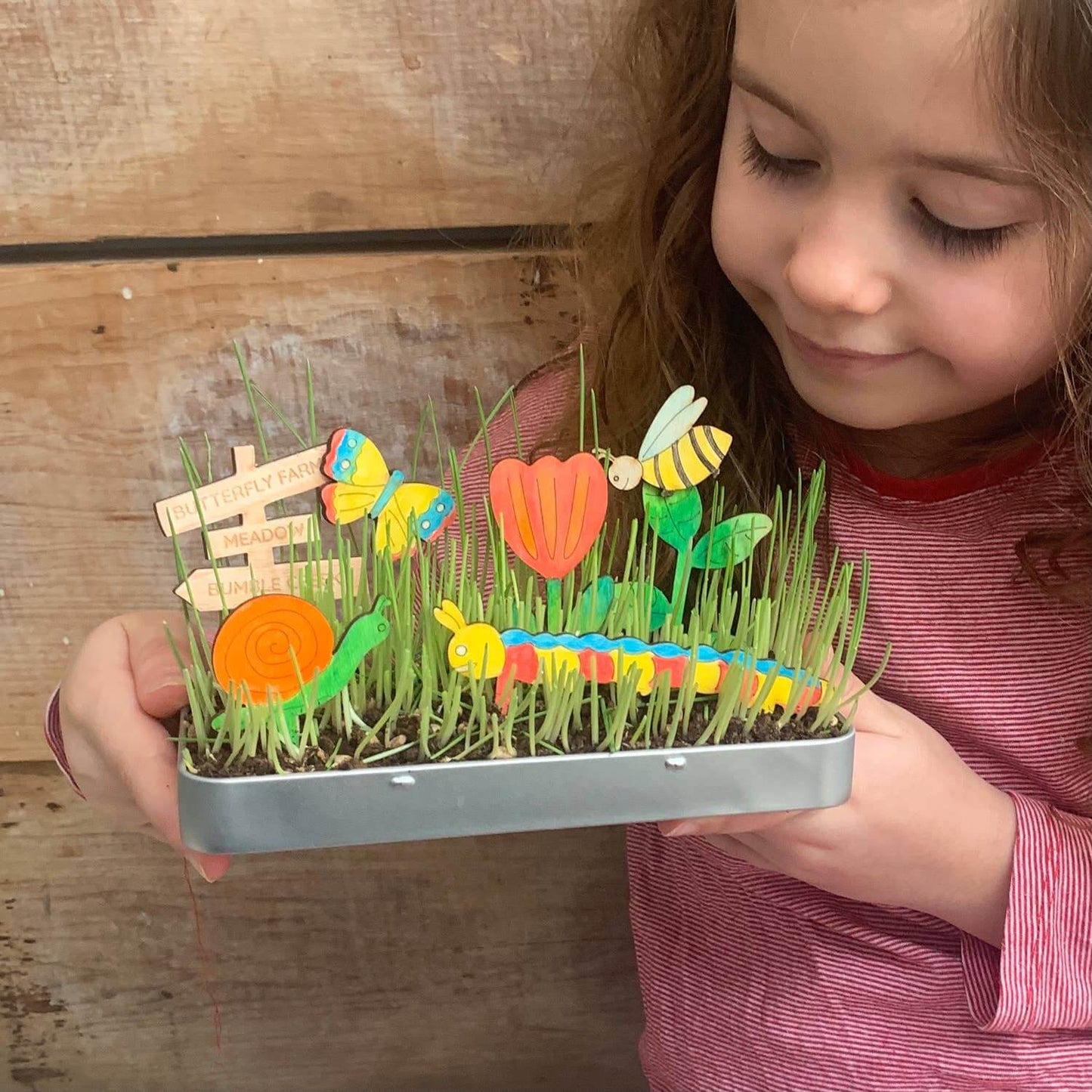 Child holding a small garden with toy plants and animals against a wooden background