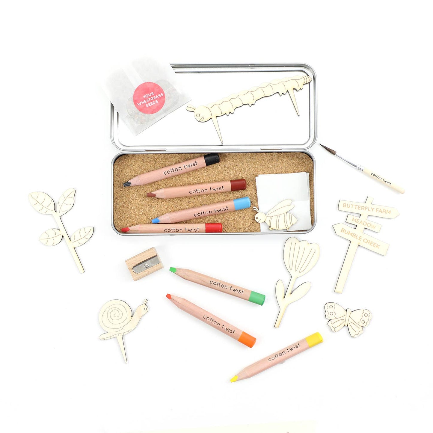 Set of items including color pencils, a sharpener, and decorative items in a tin box on a white background.