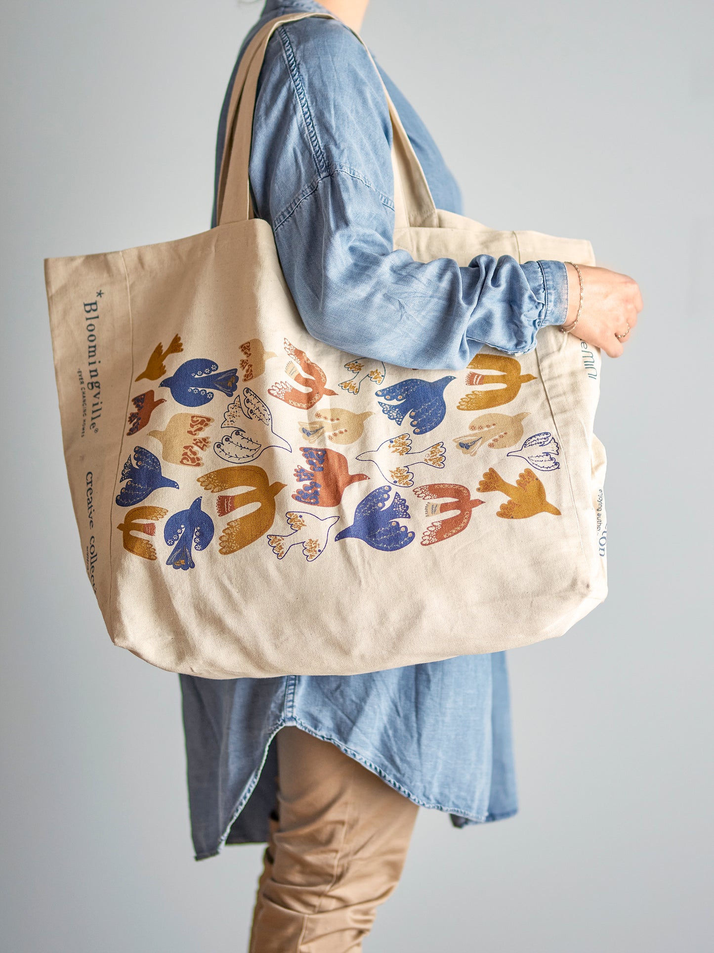 Person holding a beige tote bag with colorful fish design against a gray background