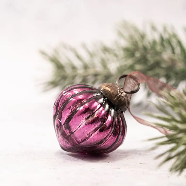 Pink glass ornament on a branch with a white background