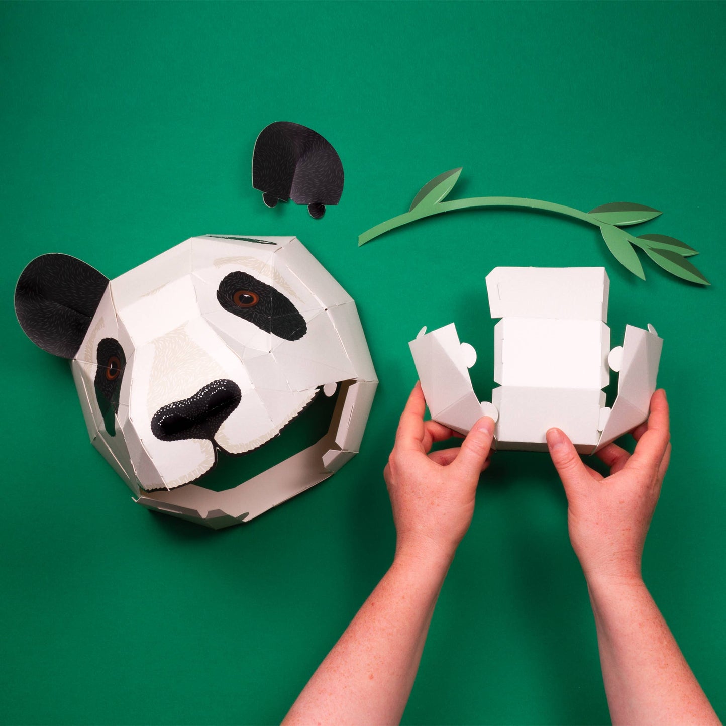 Panda-shaped paper craft with hands assembling it on a green background