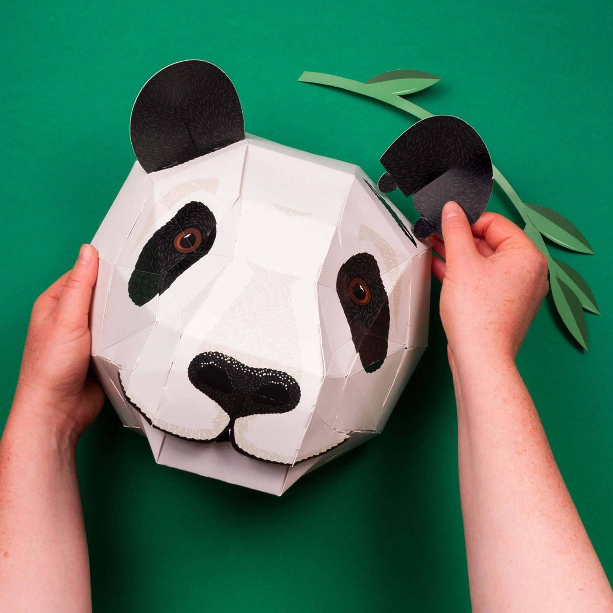 Hands holding a paper panda mask against a green background