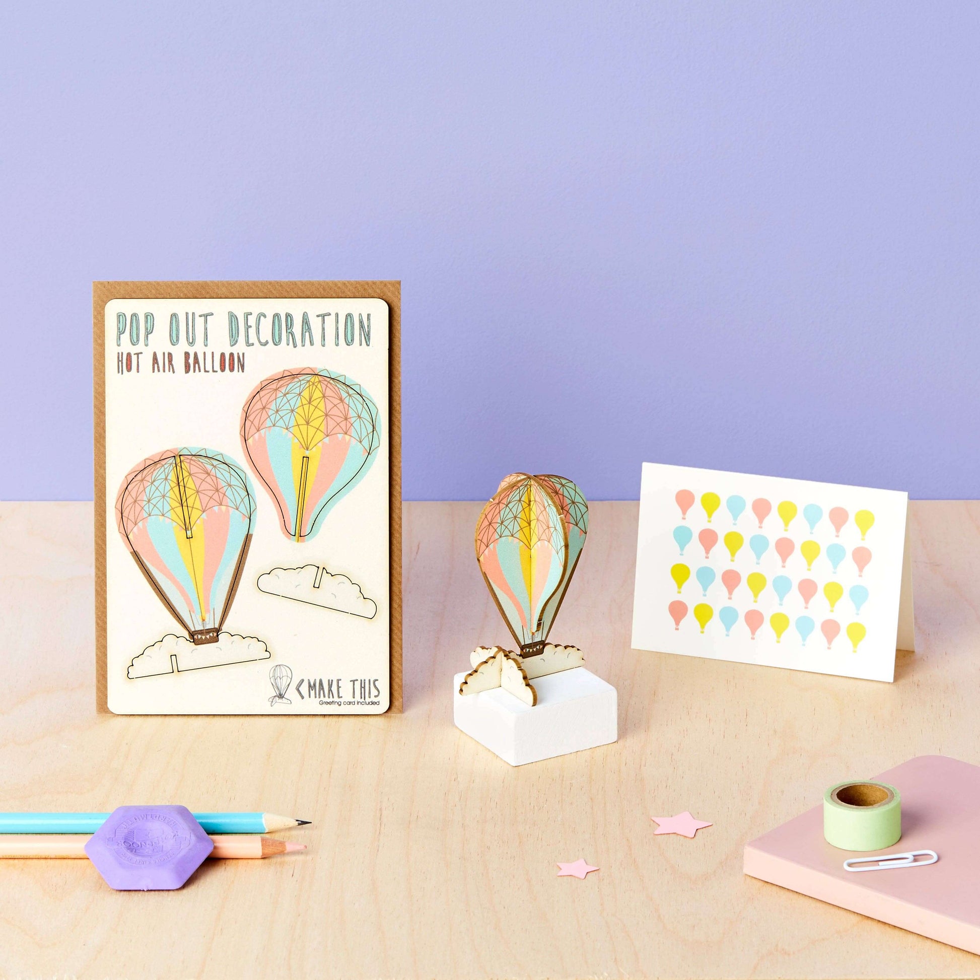 A greeting card with a pop-out hot air balloon design, accompanied by an A7 greeting card with a repeat hot air balloon pattern and a brown A6 envelope sitting on a table