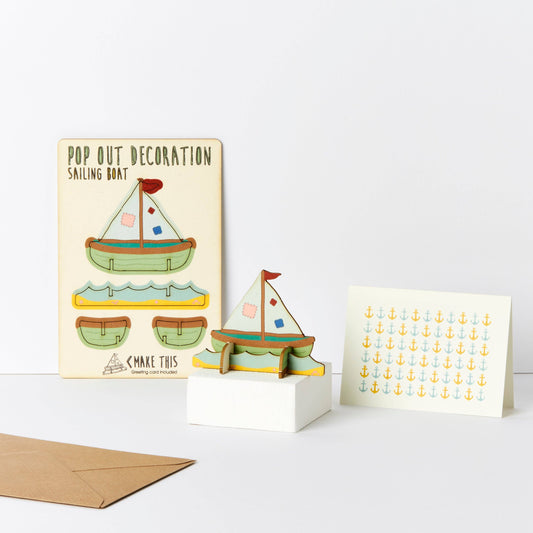 A greeting card with a pop-out sailing boat decoration and an envelope, showcasing a cartoon-style sailboat and anchor patterns.