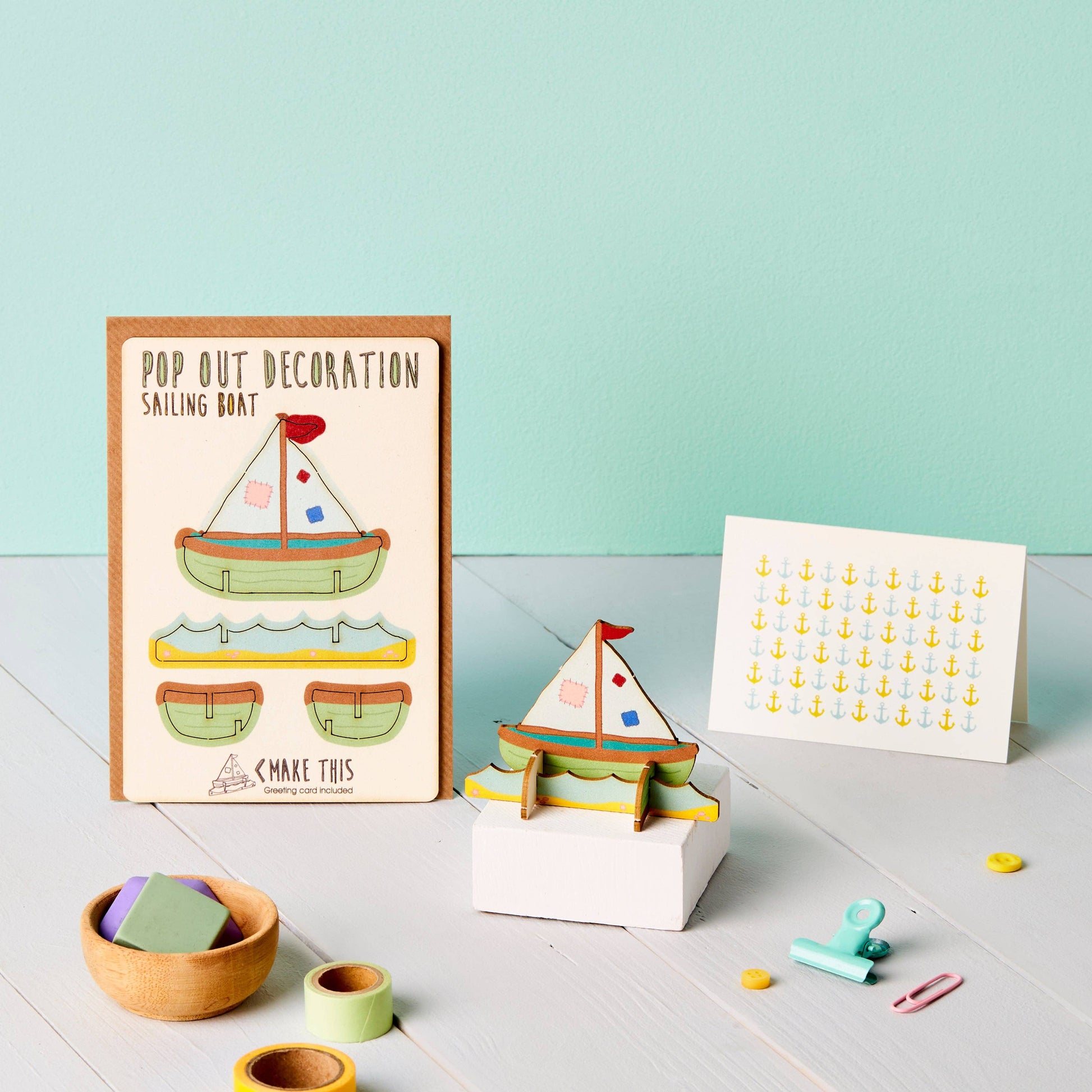 A greeting card with a pop-out sailing boat decoration and an envelope, showcasing a cartoon-style sailboat and anchor patterns sitting on a table