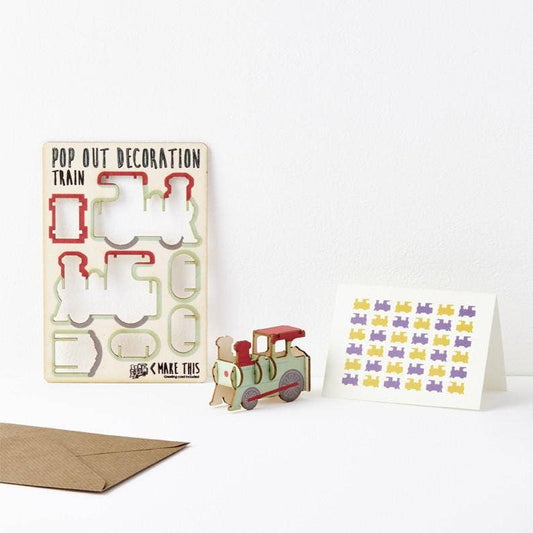 A greeting card with a 3D pop-out train design, accompanied by an A7 greeting card with a repeat train pattern and a brown A6 envelope. Both items have a cardboard train decoration with cut-out pieces.