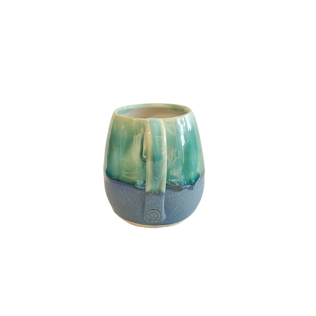 Pretty hand thrown flat white mug in dark blue and green glaze. Side view showing embossed spiral pattern at the base of the handle.