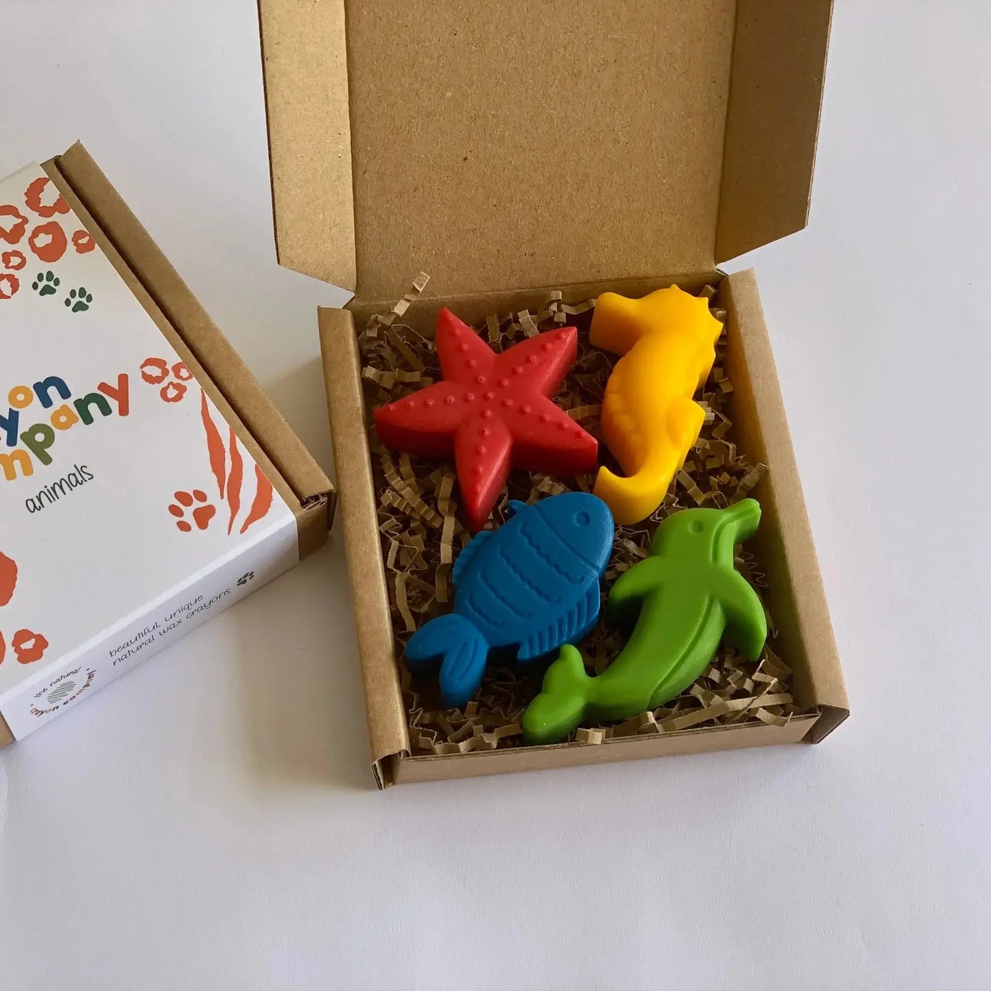 Colorful animal-shaped crayons in a box with a branded card on a white background