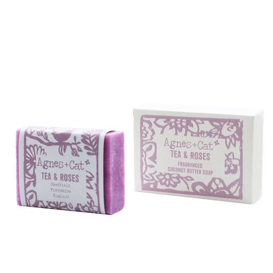 A bar of coconut butter soap with 'Tea & Roses' fragrance, embossed on the top, next to its packaging box with a floral design.