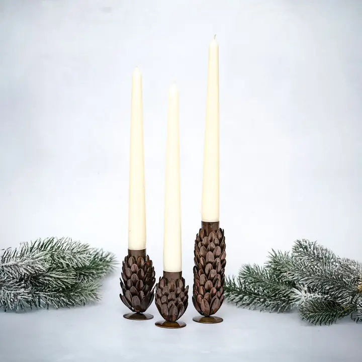 Three pine cone-shaped candle holders with candles on a snowy background