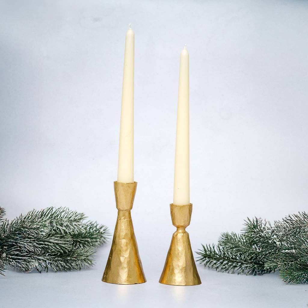 Two gold coloured candle holders on white background with festive greenery