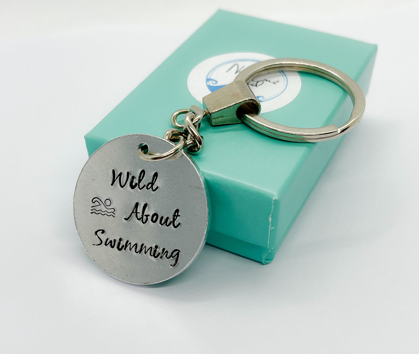 Metal disc key ring hand- stamped with "Wild About Swimming" and a simple graphic of a swimmer in water.