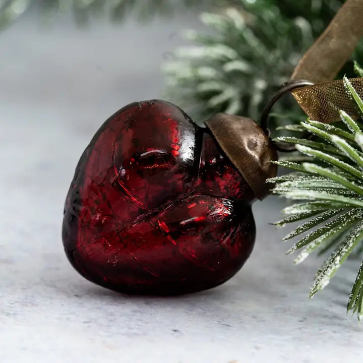 Red glass heart ornament on a branch with a blurred background
