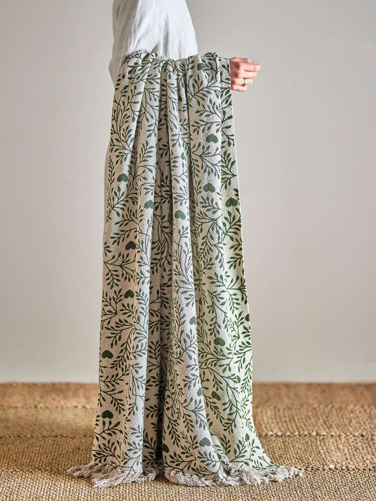 Floral-patterned throw being held up against a neutral background