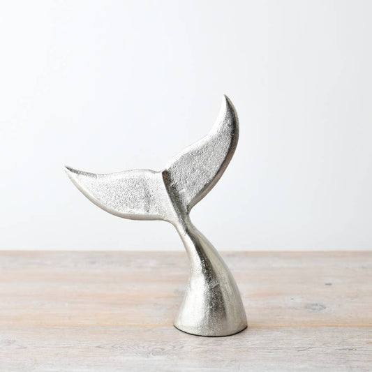 Metallic silver whale tail sculpture on a light wooden surface with a white background
