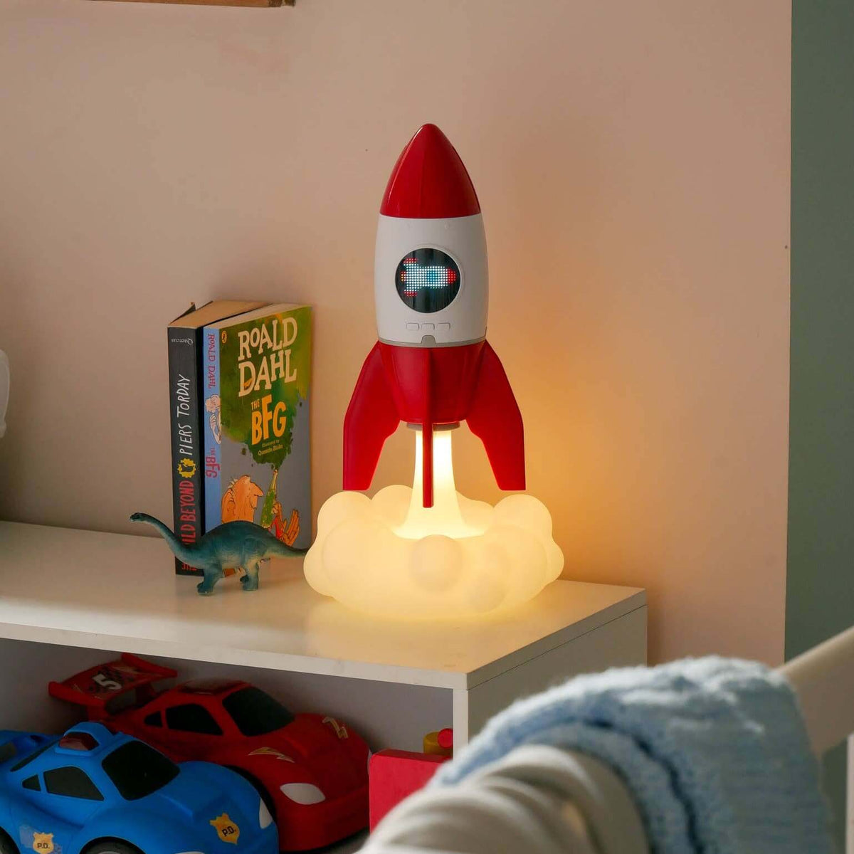 Rocket-shaped night light on a shelf with children's books and toys in a room.