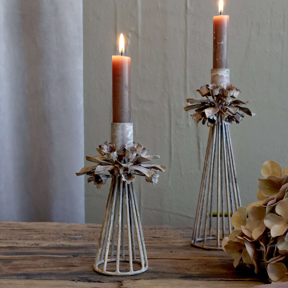 Two candle holders with candles on a wooden surface against a neutral background