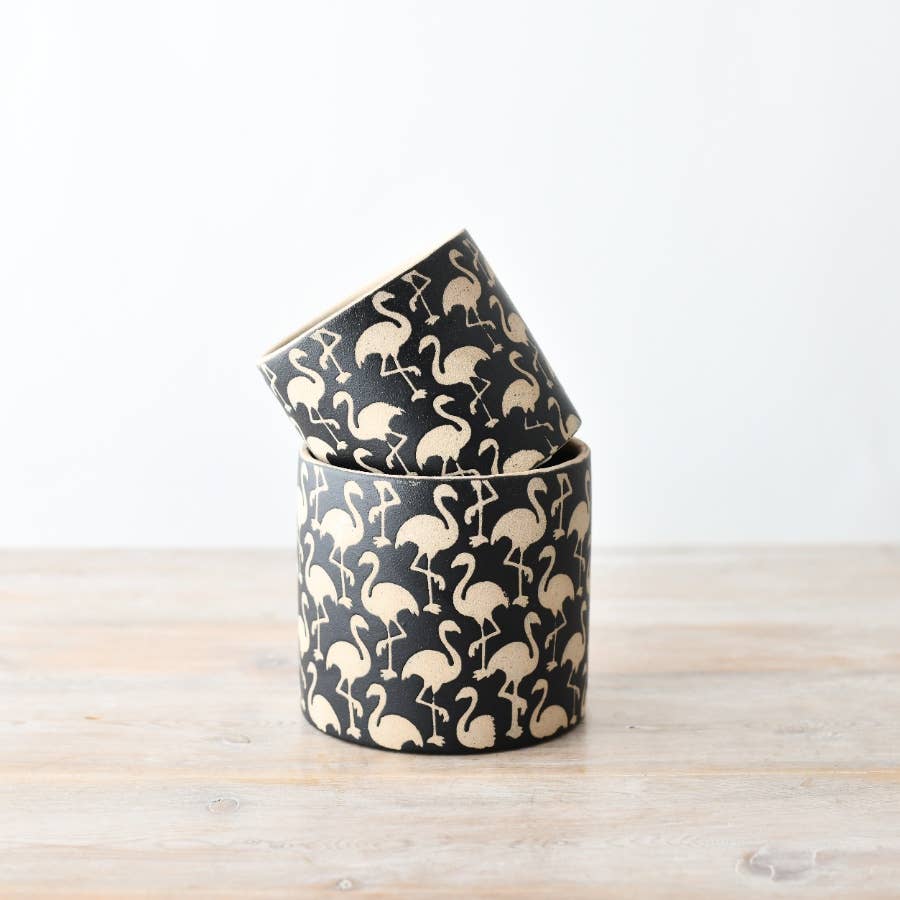 A cylindrical stoneware planter with black and cream flamingo pattern detailing, placed on a wooden surface.