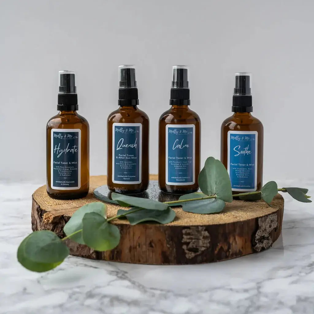 Four brown spray bottles with blue labels on a wooden stand with eucalyptus leaves.