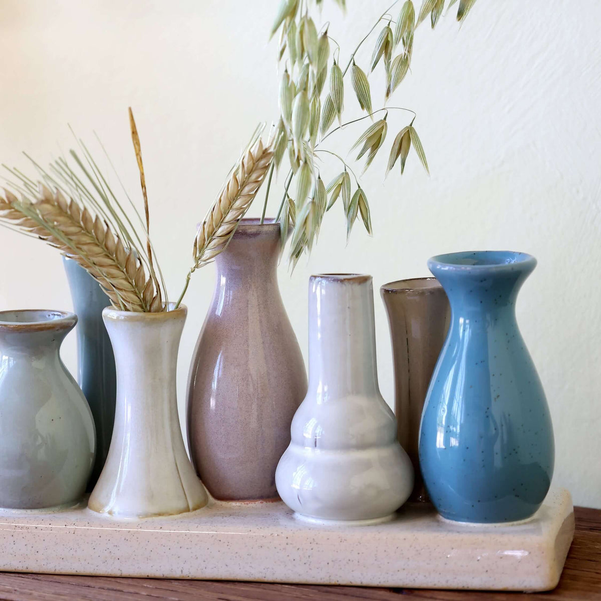 Side view of a tray of mini ceramic vases with decorative grass