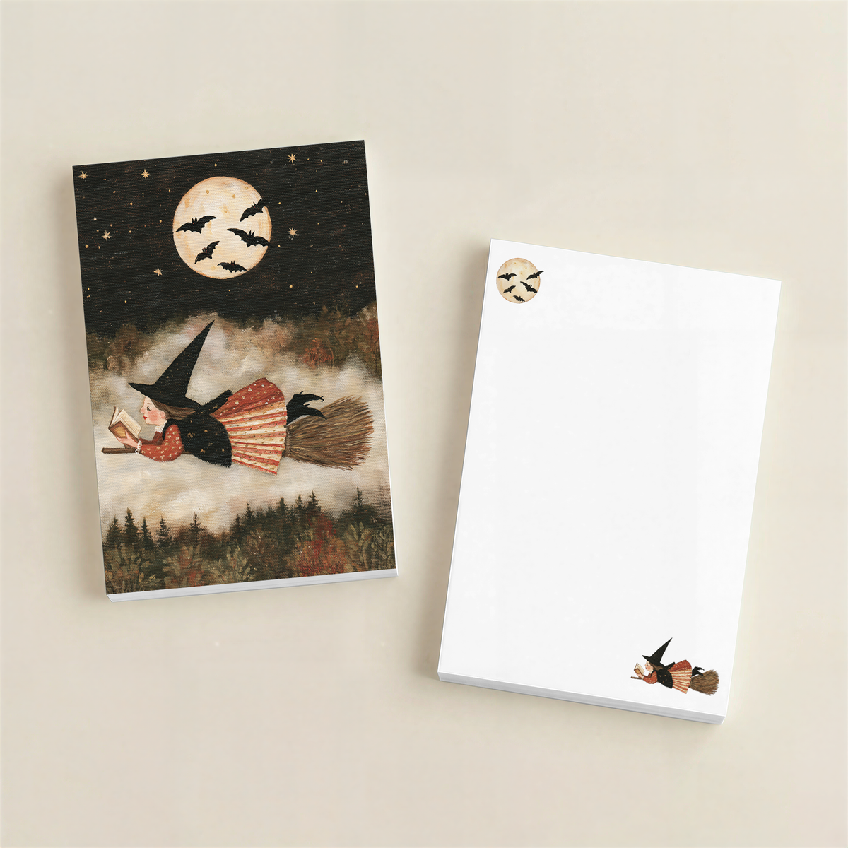 A Halloween-themed notepad set on a warm beige background, featuring a printed cover illustration of a witch riding a broomstick under a full moon with bats, alongside a blank white notepad with matching small witch illustrations.
