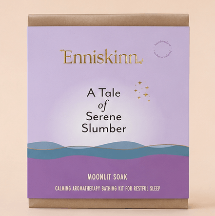 A boxed bath kit package for 'Enniskinn A Tale of Serene Slumber Moonlit Soak' shown against a solid beige background. The box features a lavender and purple gradient cover with gold foil branding and a wavy blue and purple landscape design, framed by brown kraft paper borders at the top and bottom.