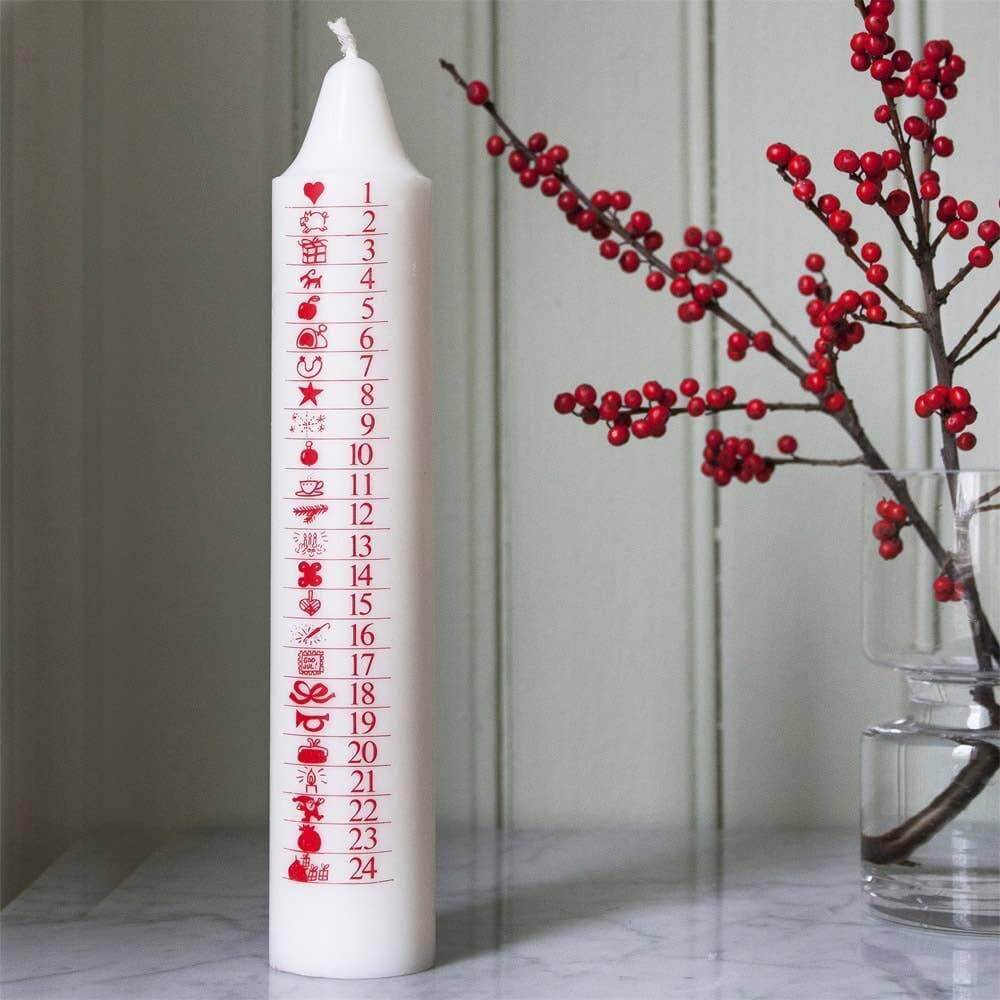 White candle with red numbering and designs next to a branch with red berries on a marble surface.