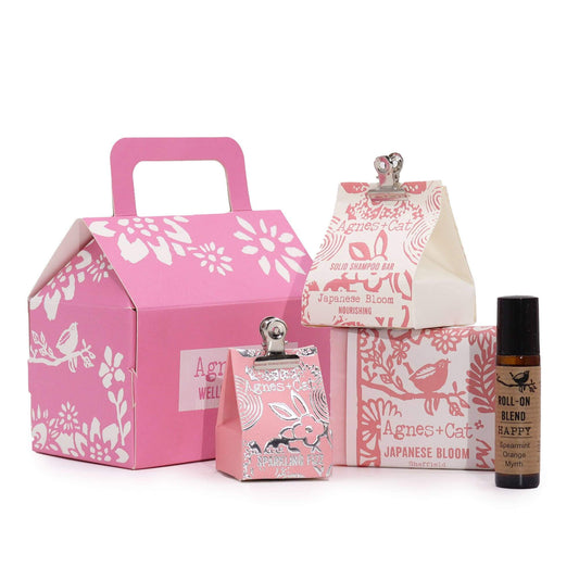 A wellness gift set including a coconut butter soap, solid shampoo, lip balm, and a roll-on essential oil, all with floral packaging themes.