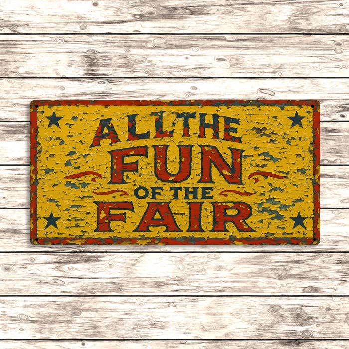 Vintage-style sign with 'All the Fun of the Fair' text on a wooden background