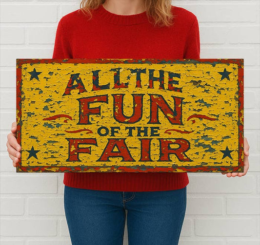 Person holding a vintage-style sign with 'All the Fun of the Fair' text against a white brick wall.