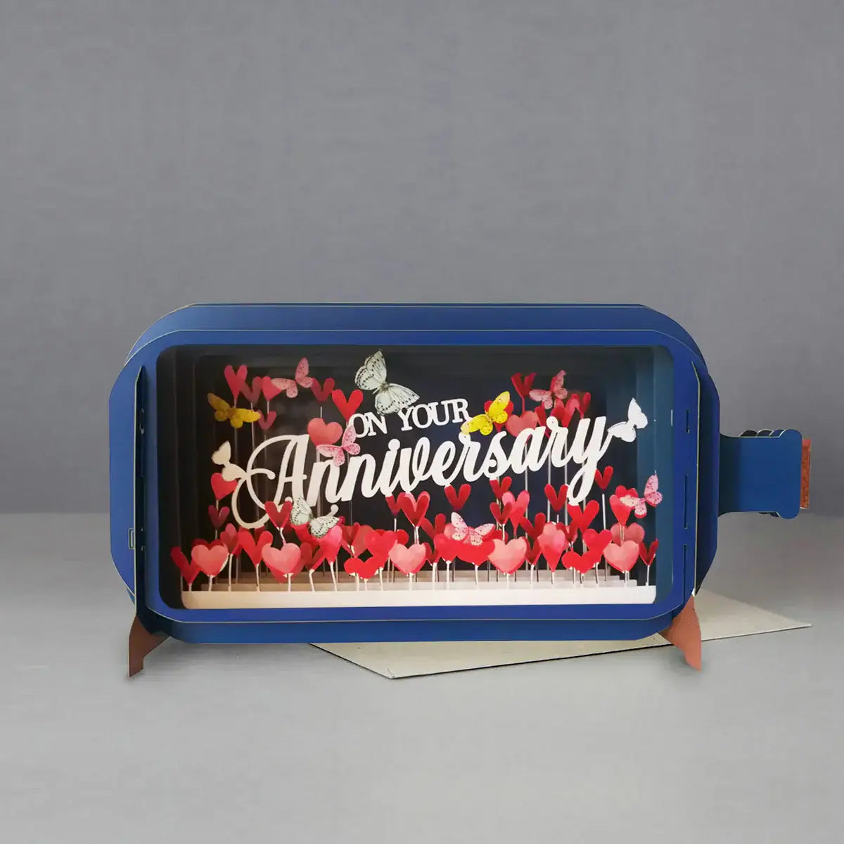 A 3D pop-up greeting card with the message 'On Your Anniversary' displayed inside a bottle design, accompanied by red and pink butterfly cut-outs.