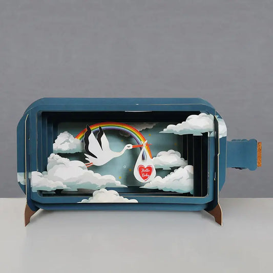 A 3D pop-up greeting card depicting a stork delivering a message, surrounded by clouds and a rainbow.