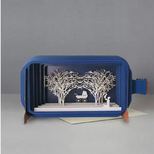 A blue pop-up greeting card displayed open with a design featuring a mother and baby with trees in the background.