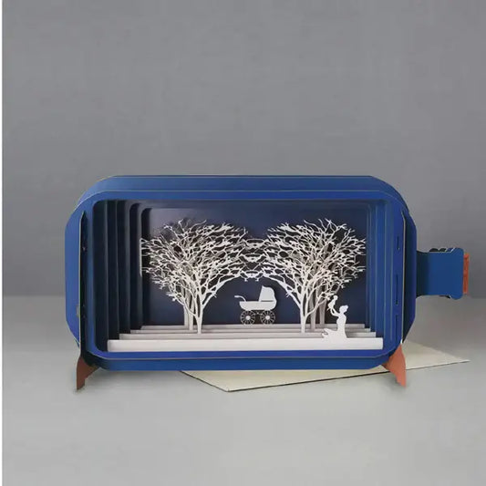 A blue pop-up greeting card displayed open with a design featuring a mother and baby with trees in the background.