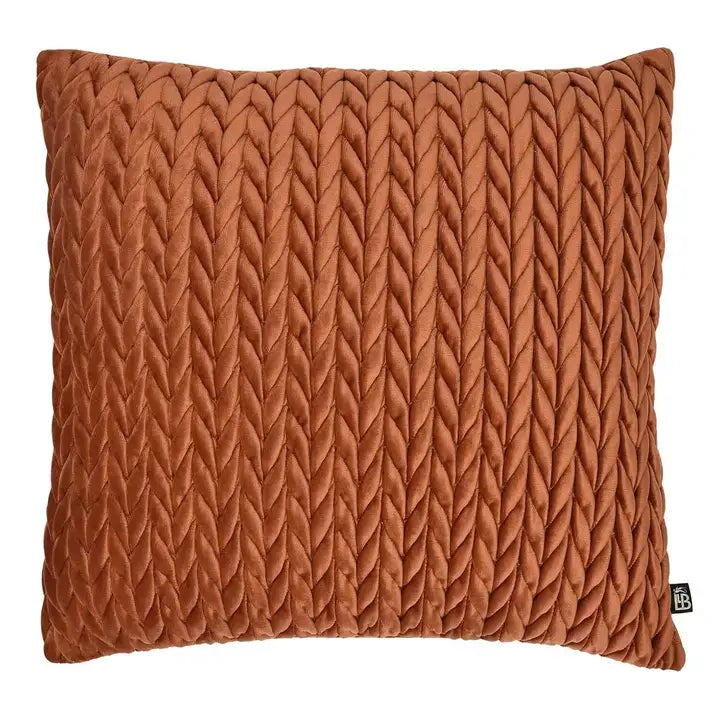 A square throw pillow in a warm rust-orange color, featuring a prominent vertical textured chevron or braided knit pattern, shown against a plain white background.